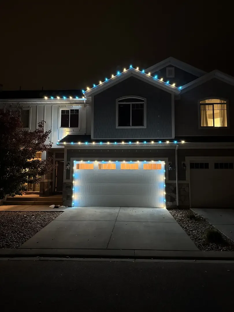 Blue and white Christmas lighting installed along roofline and garage